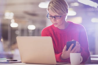 Woman holding phone and looking at laptop